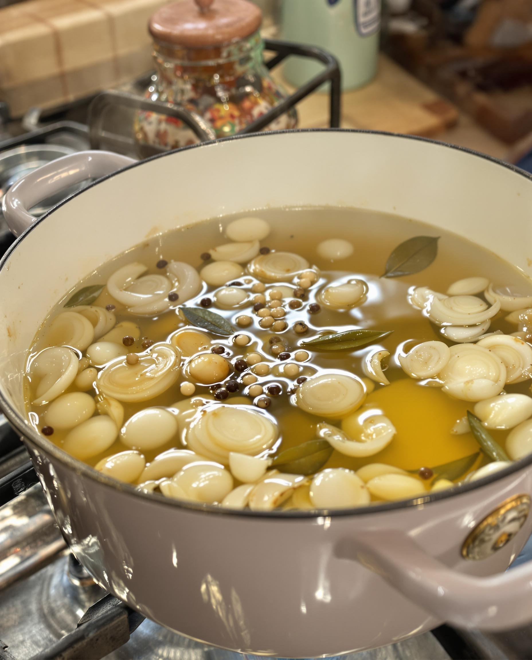 Casserole émaillée blanche contenant vinaigre blanc et vin blanc frémissant doucement avec échalotes, grains de poivre et laurier.