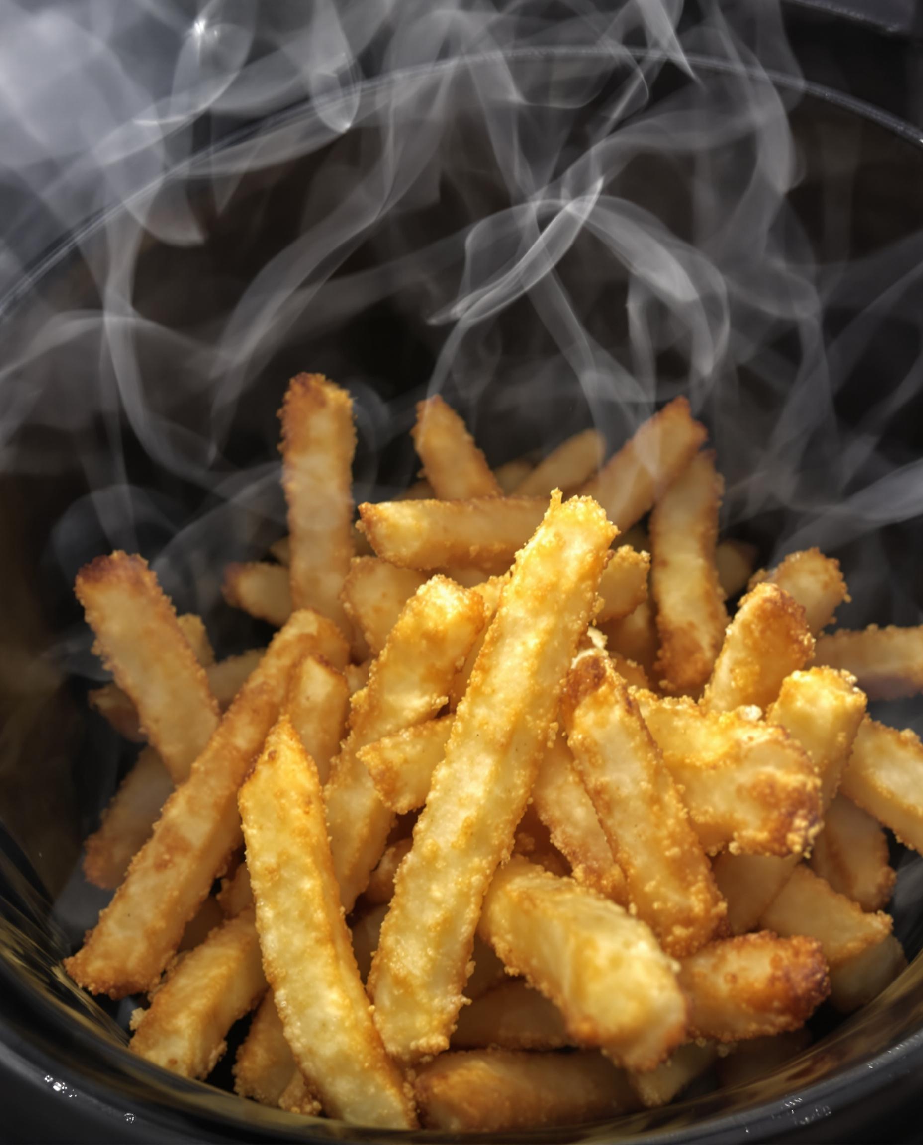 Gros plan sur des frites surgelées devenues ultra-croustillantes grâce à la convection rapide de l’Airfryer, panier noir brillant en contraste. Vapeur visible, aspect doré et appétissant.